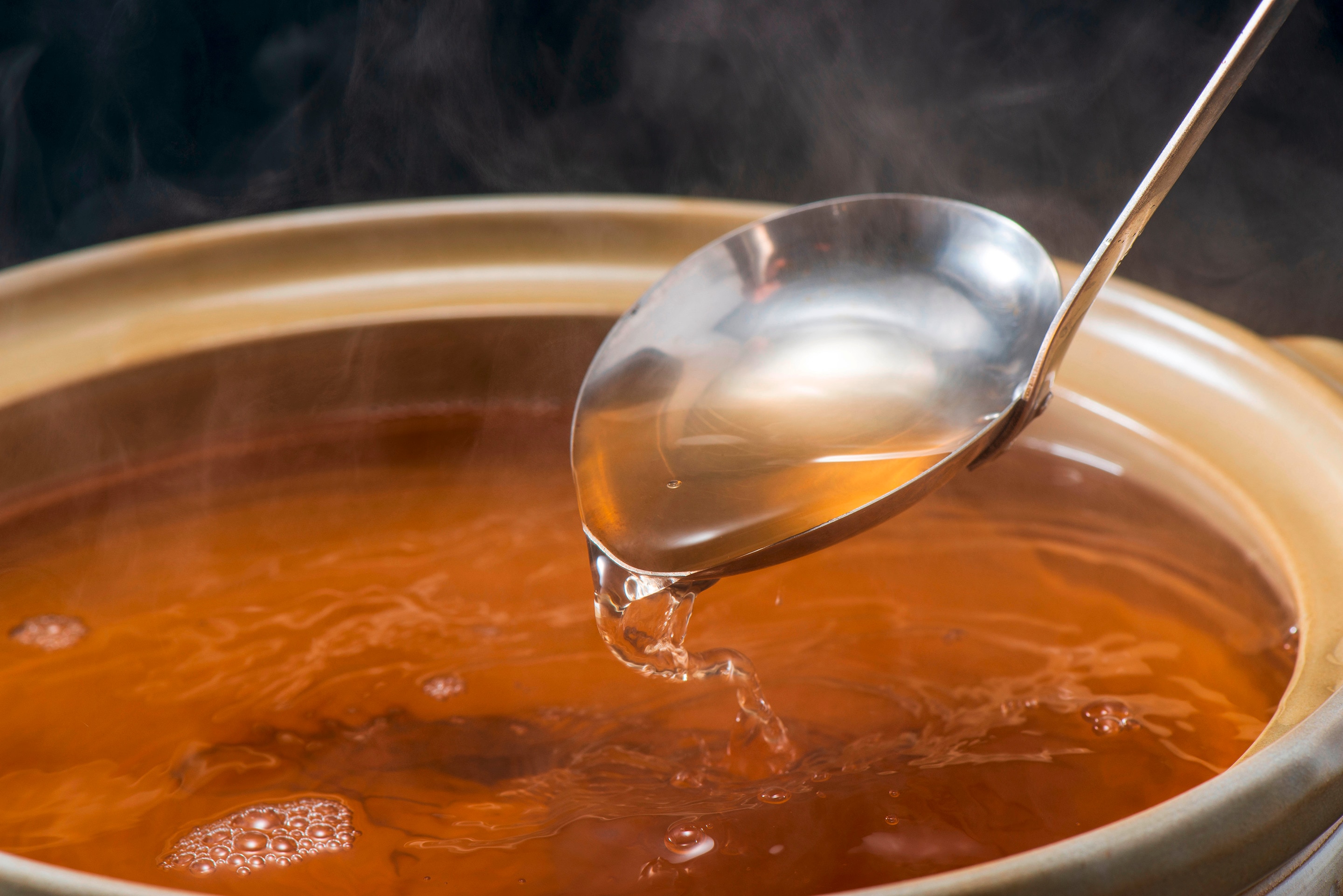 A pot filled with hot fish soup with a metal ladle scooping a portion