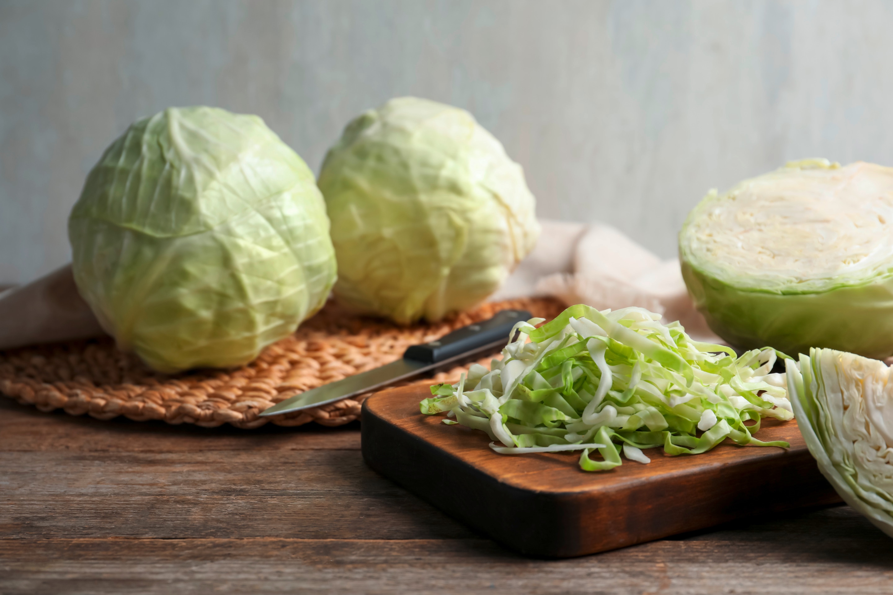 Two whole cabbages along with half a head and some shredded on a chopping board