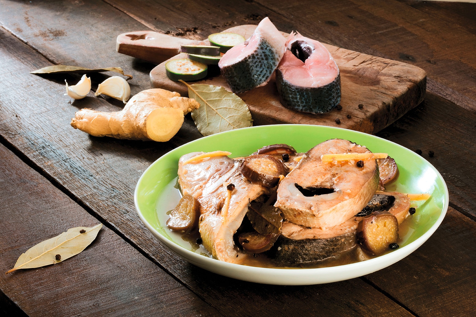 A bowl of paksiw na bangus beside a chopping board with raw milkfish slices and ginger
