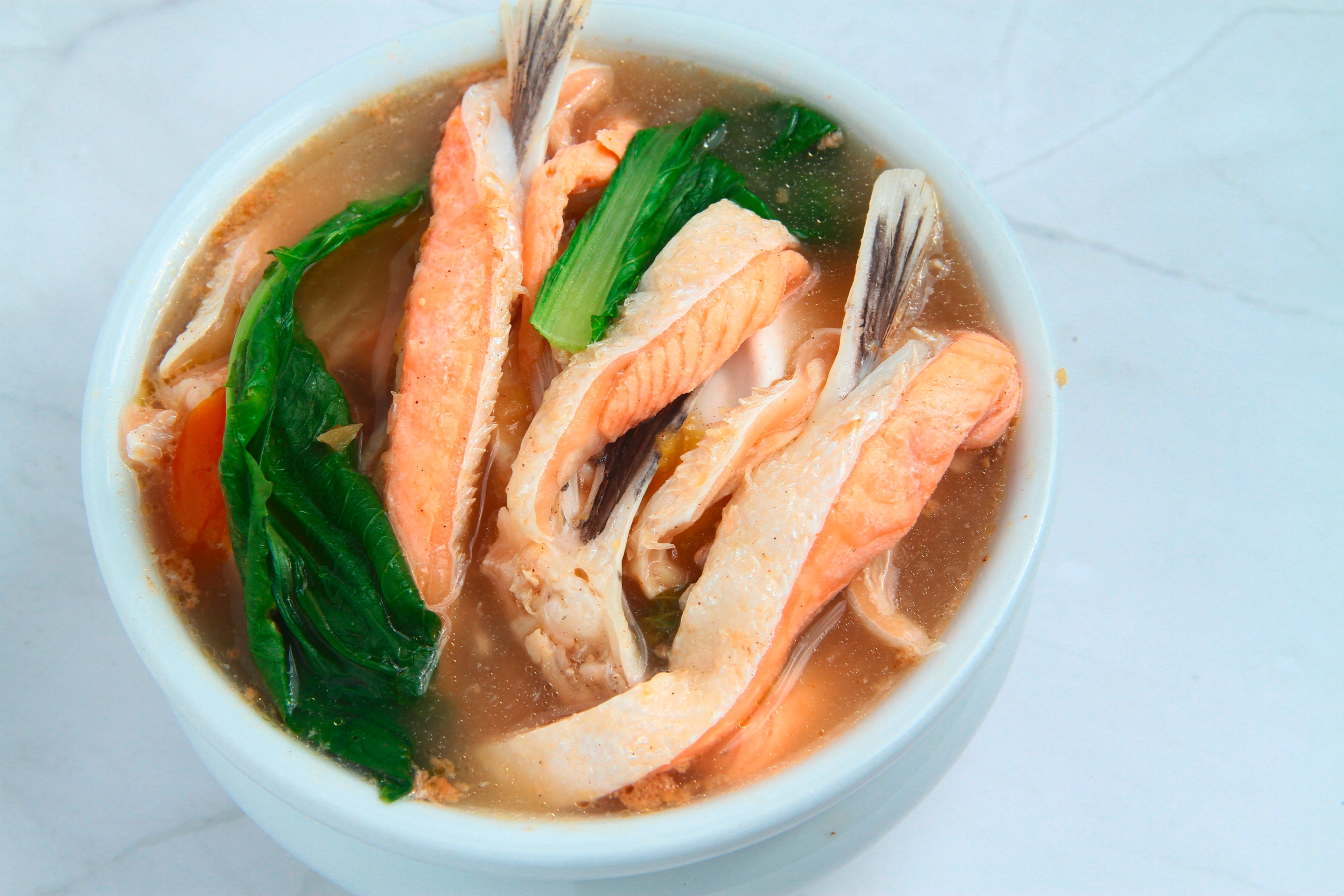 A bowl of sinigang na salmon filled with salmon steaks, kangkong, tomatoes, onions