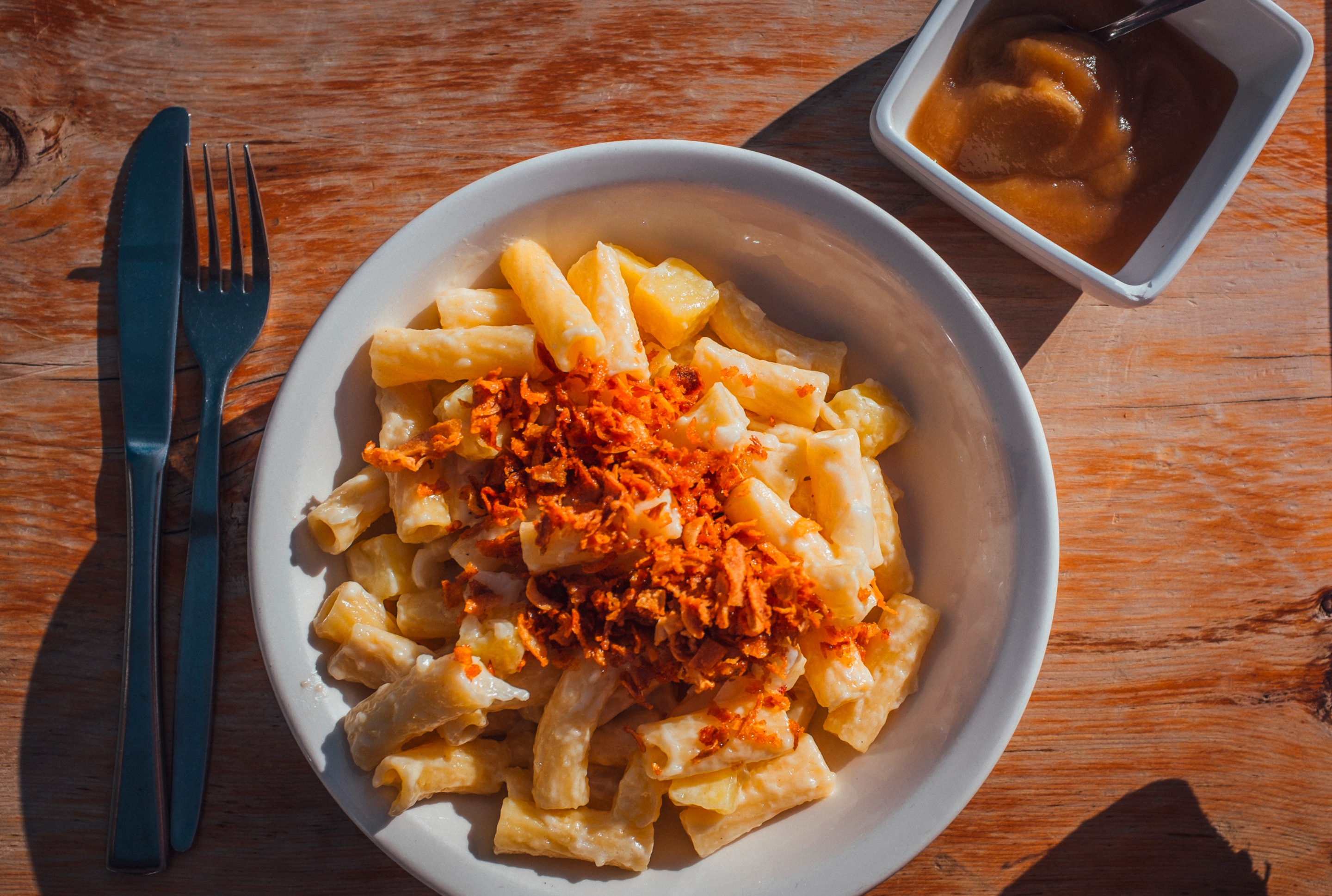 A plate of alpine macaroni garnished with bacon bits and served with a side of apple sauce