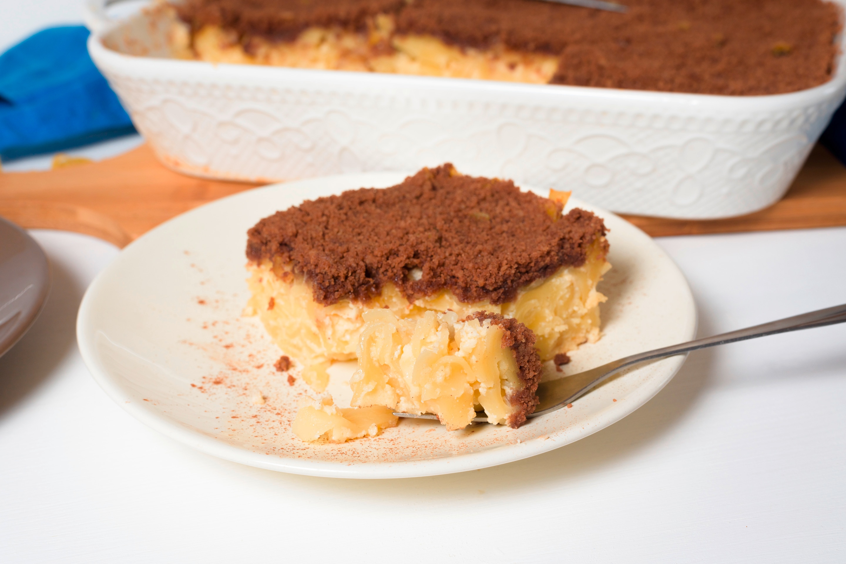 A thick slice of kugel topped with crushed graham crackers and cinnamon powder