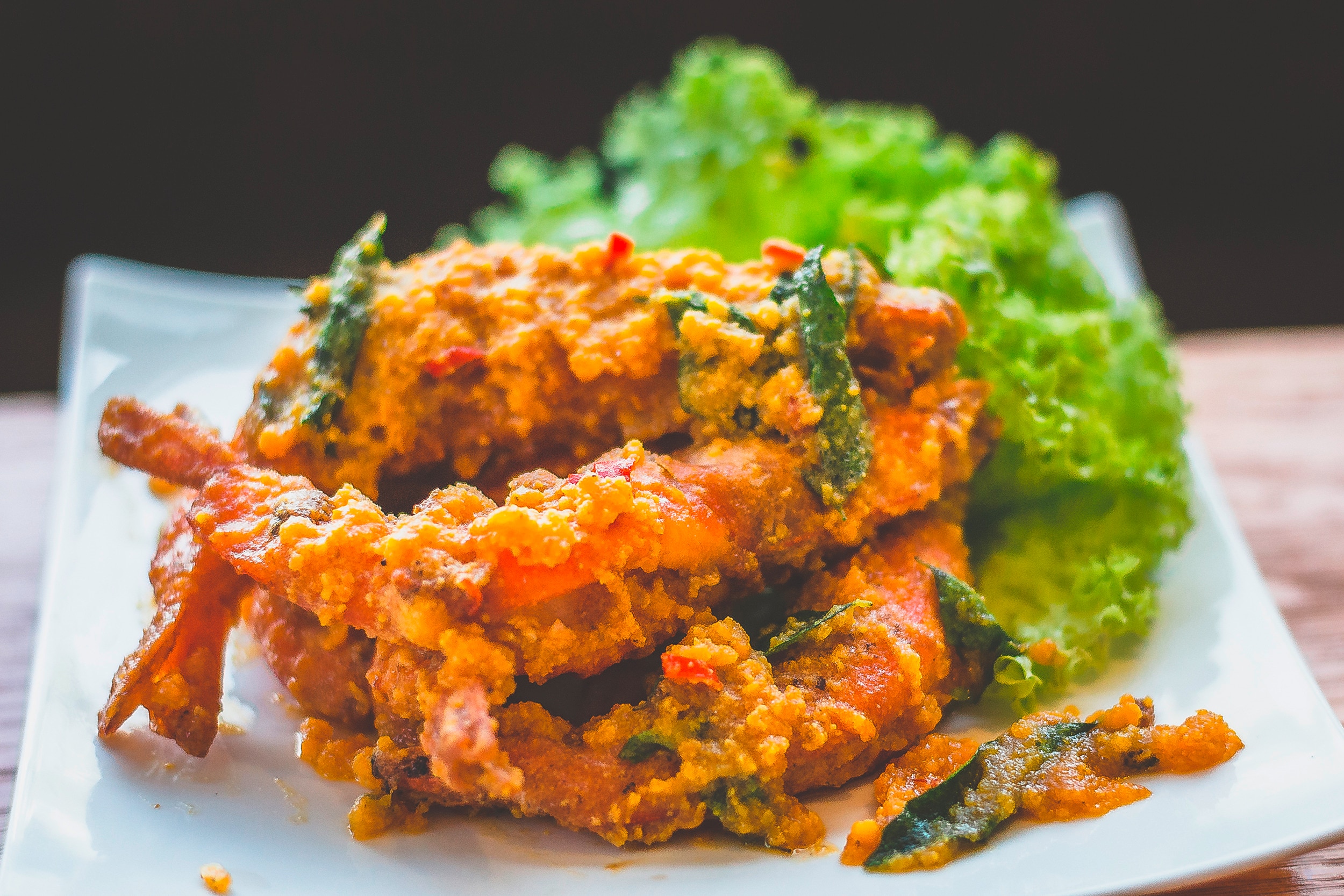 A serving of fried prawns covered in salted egg yolk sauce, basil, and chili