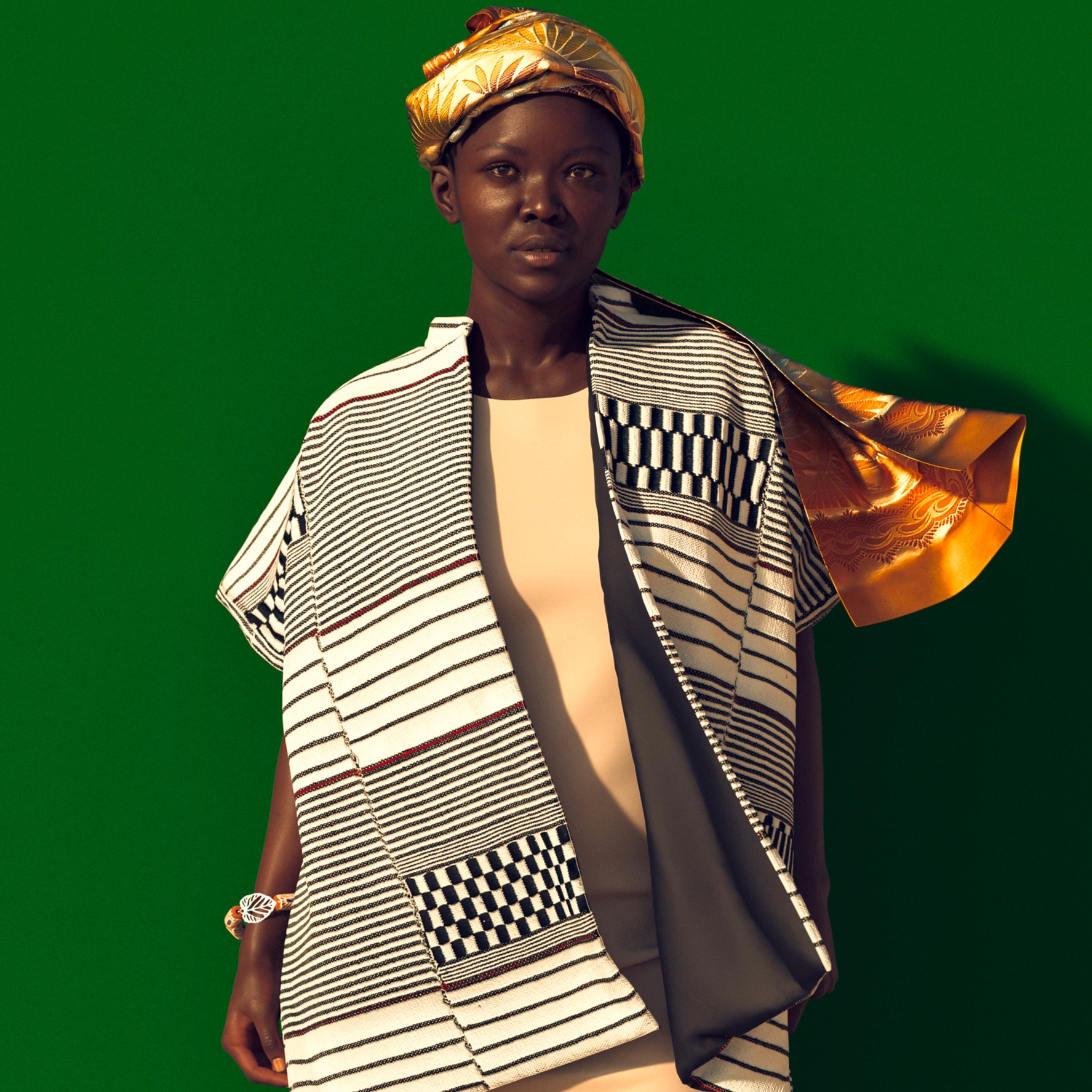 Fotografía del cuerpo de una mujer africana sobre fondo verde llevando una capa Kamandje