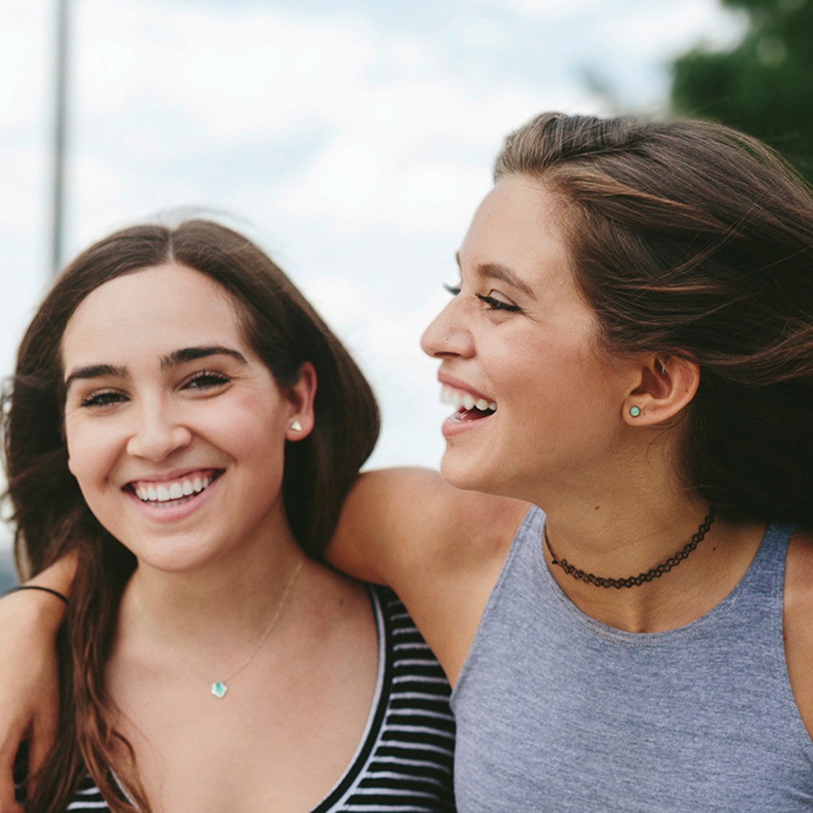 Due modelle con capelli morbidi si abbracciano e sorridono.