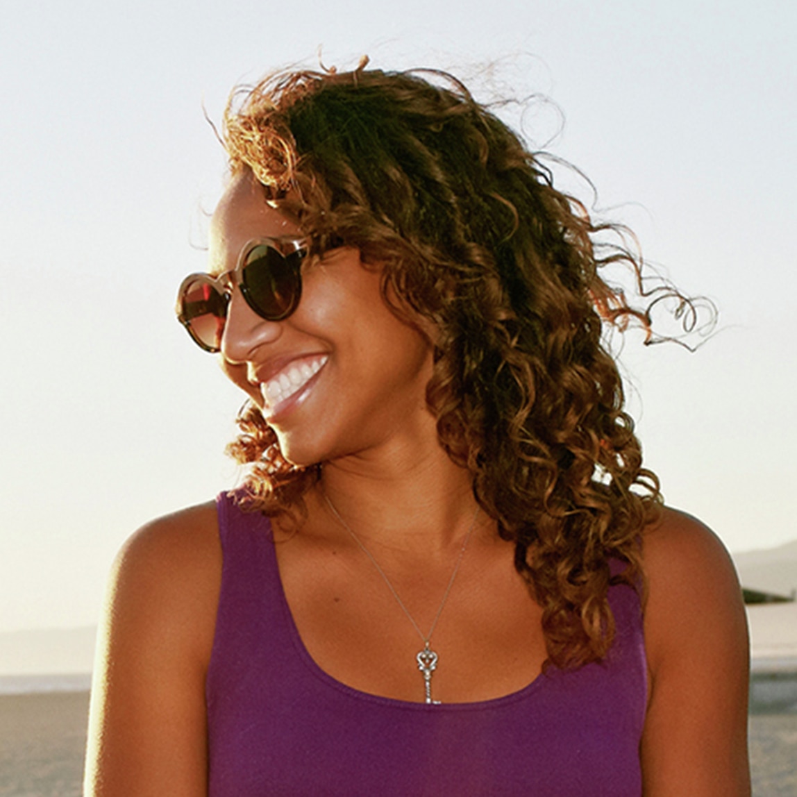 امرأة مبتسمة ذات شعر مجعد ترتدي نظارات شمسية