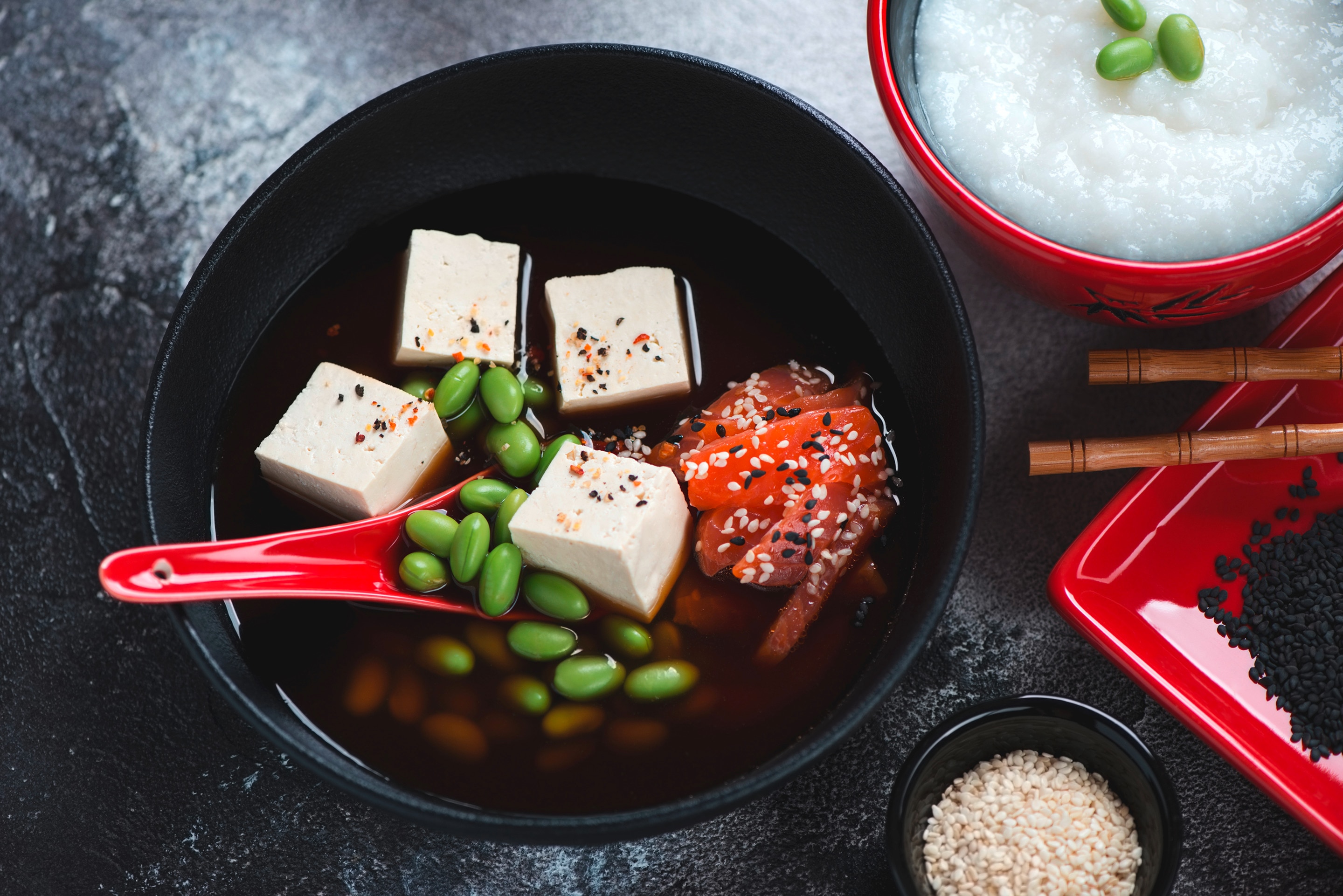 A bowl of tofu and edamame soup next to a serving of porridge topped with edamame