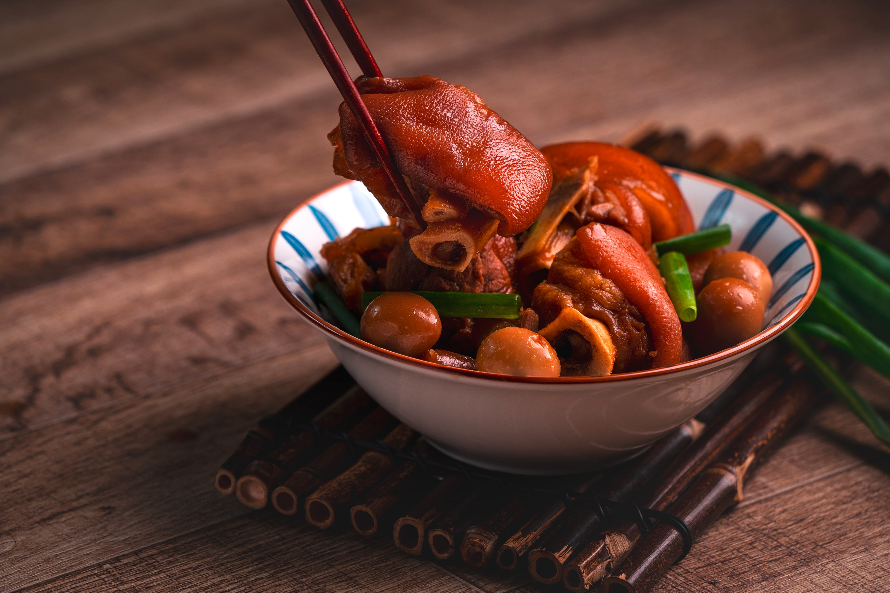 Sticky stewed ham hocks in a bowl with a piece lifted using chopsticks