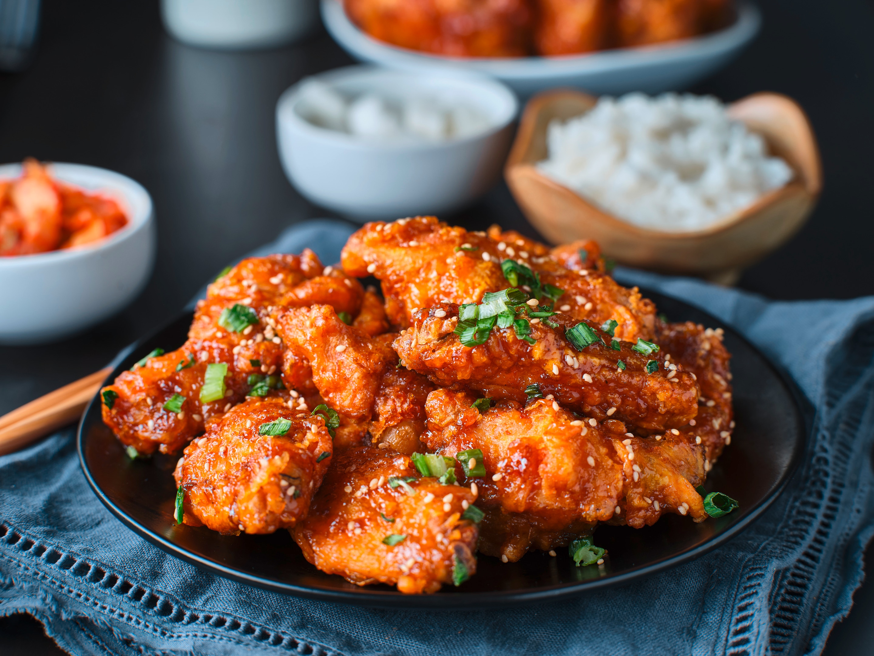 Korean fried chicken on a black plate garnished with sesame seeds and spring onion
