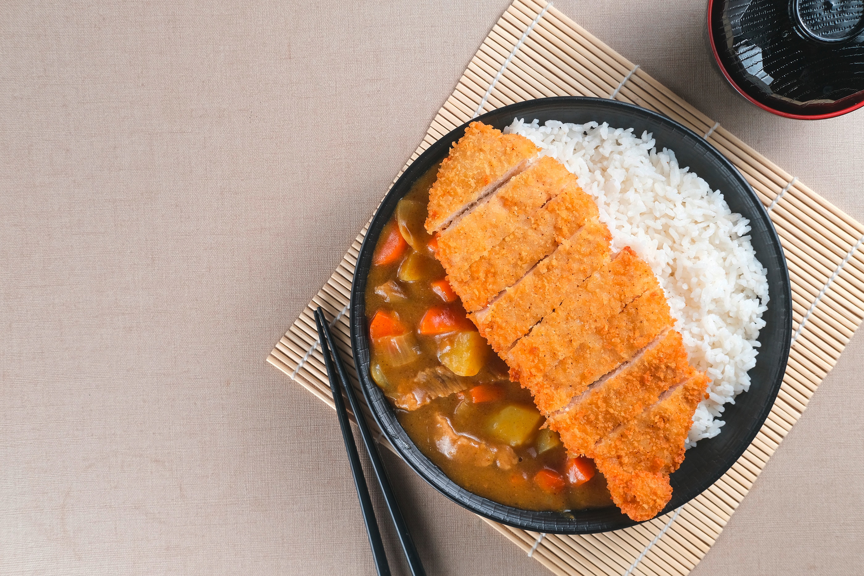 Chicken katsu curry served with rice in a black bowl on a bamboo mat