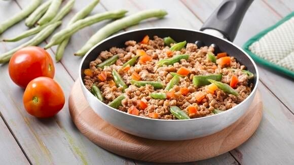 A pan with stir-fried ground pork, carrots, tomatoes, and long beans