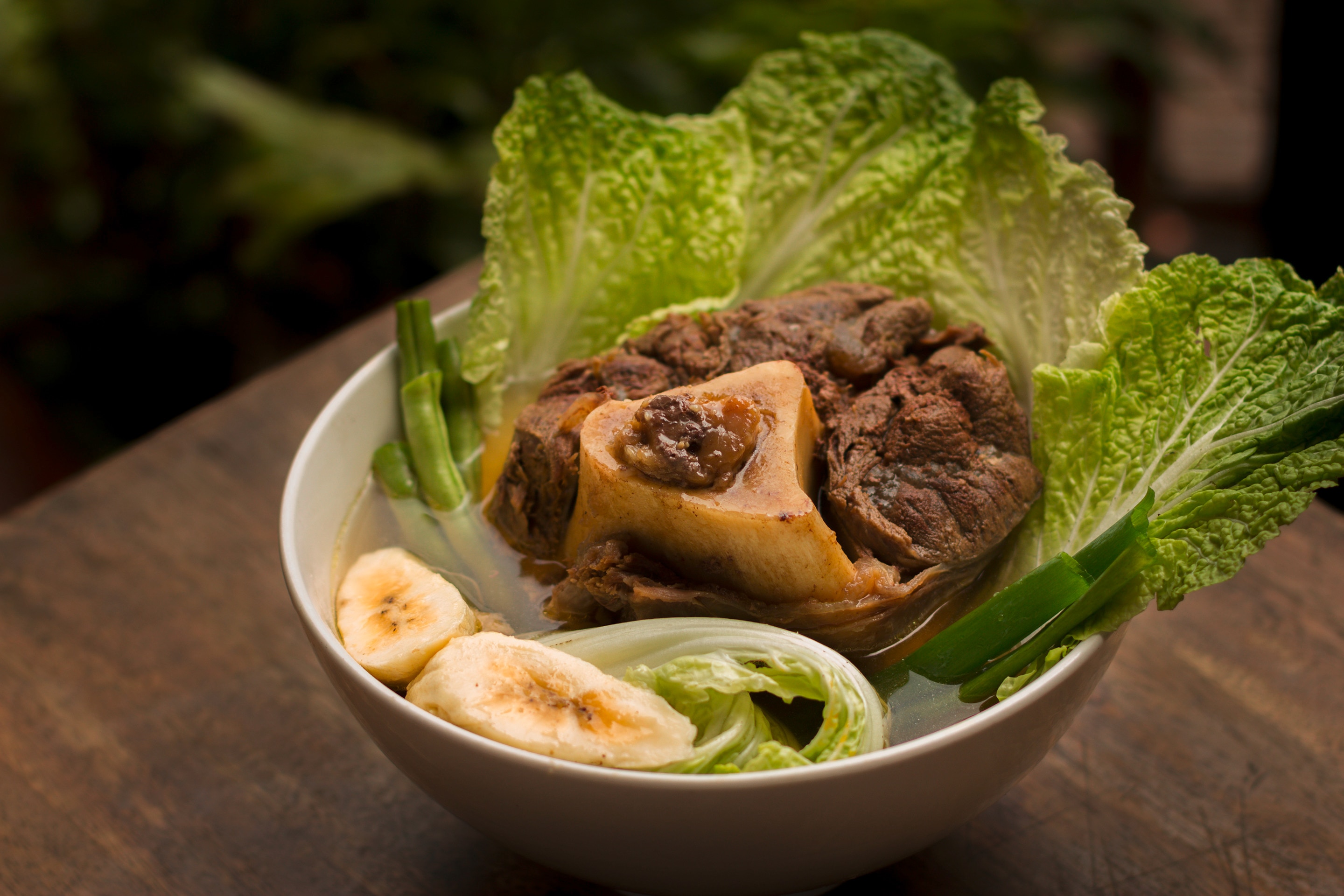 A bowl of beef pochero with beef shanks, saba bananas, and cabbage