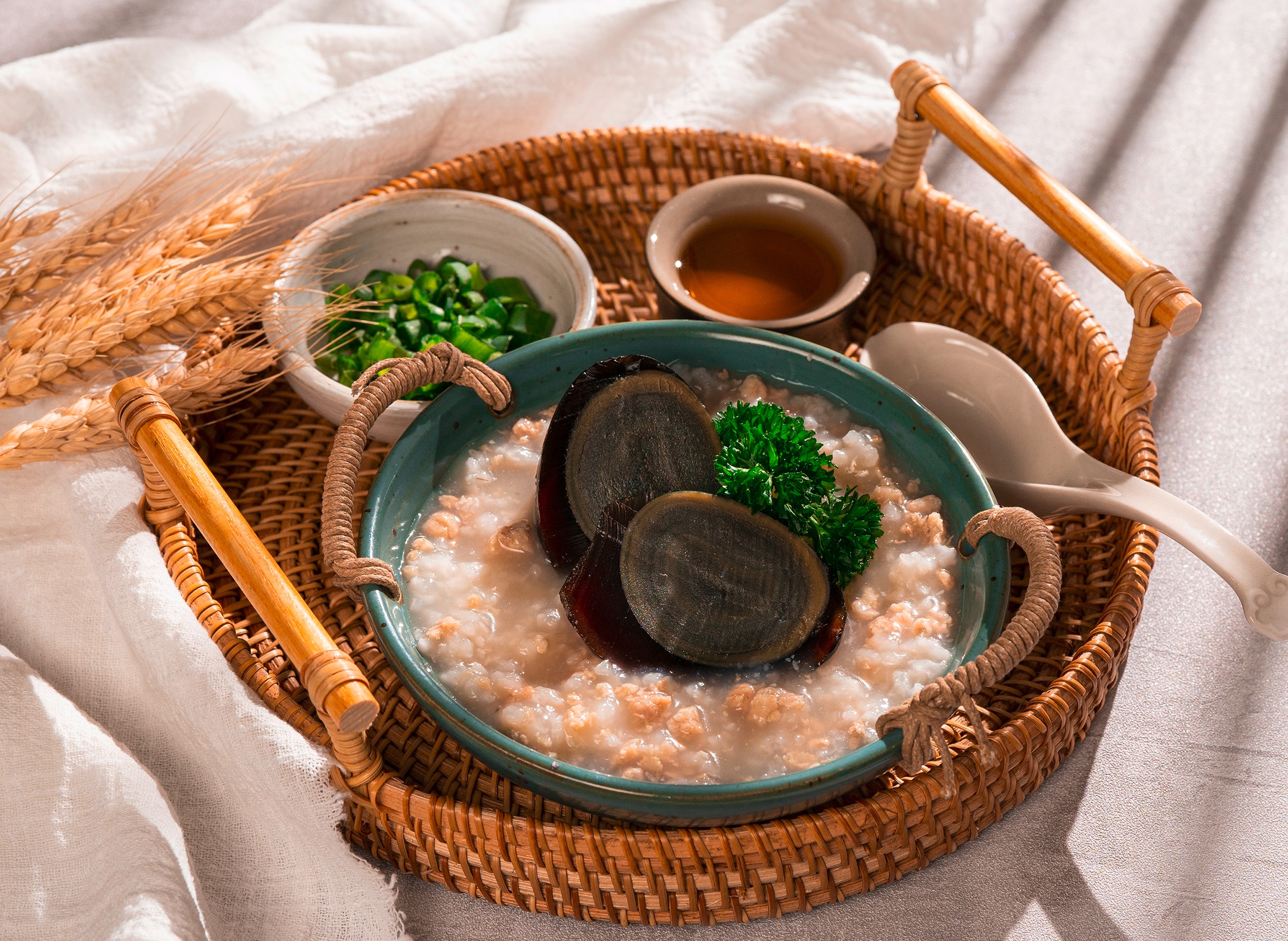 Chunky congee with halves of century eggs served on a round wicker tray