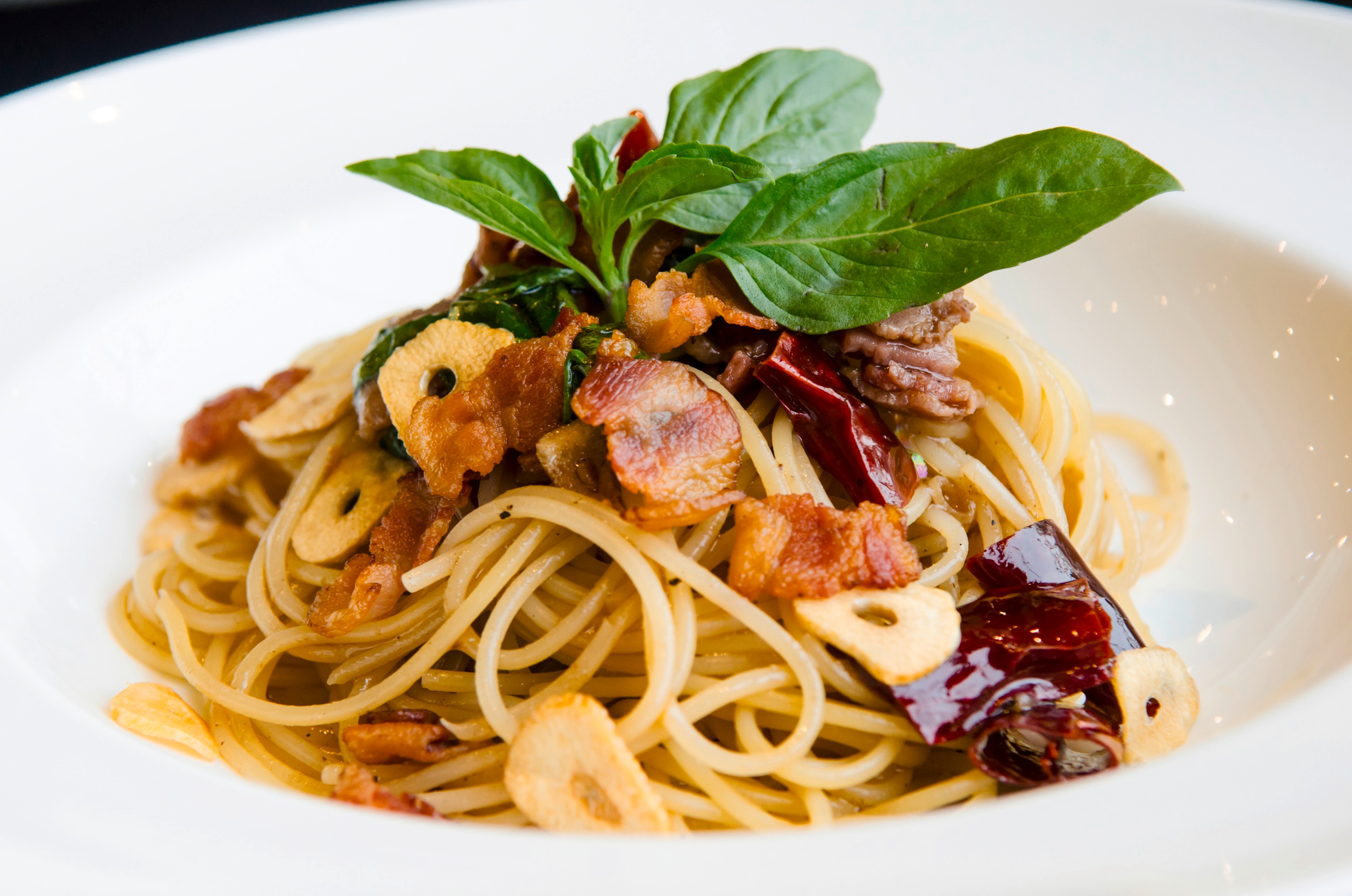 Spaghetti with crispy ham, garlic, and basil served on a white plate