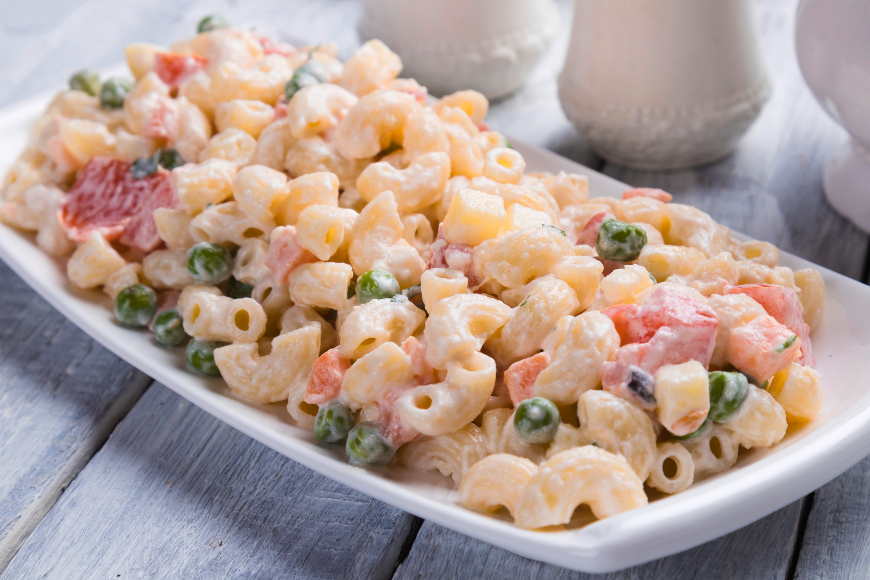 Creamy elbow macaroni salad with ham, carrots, and green peas on a white plate
