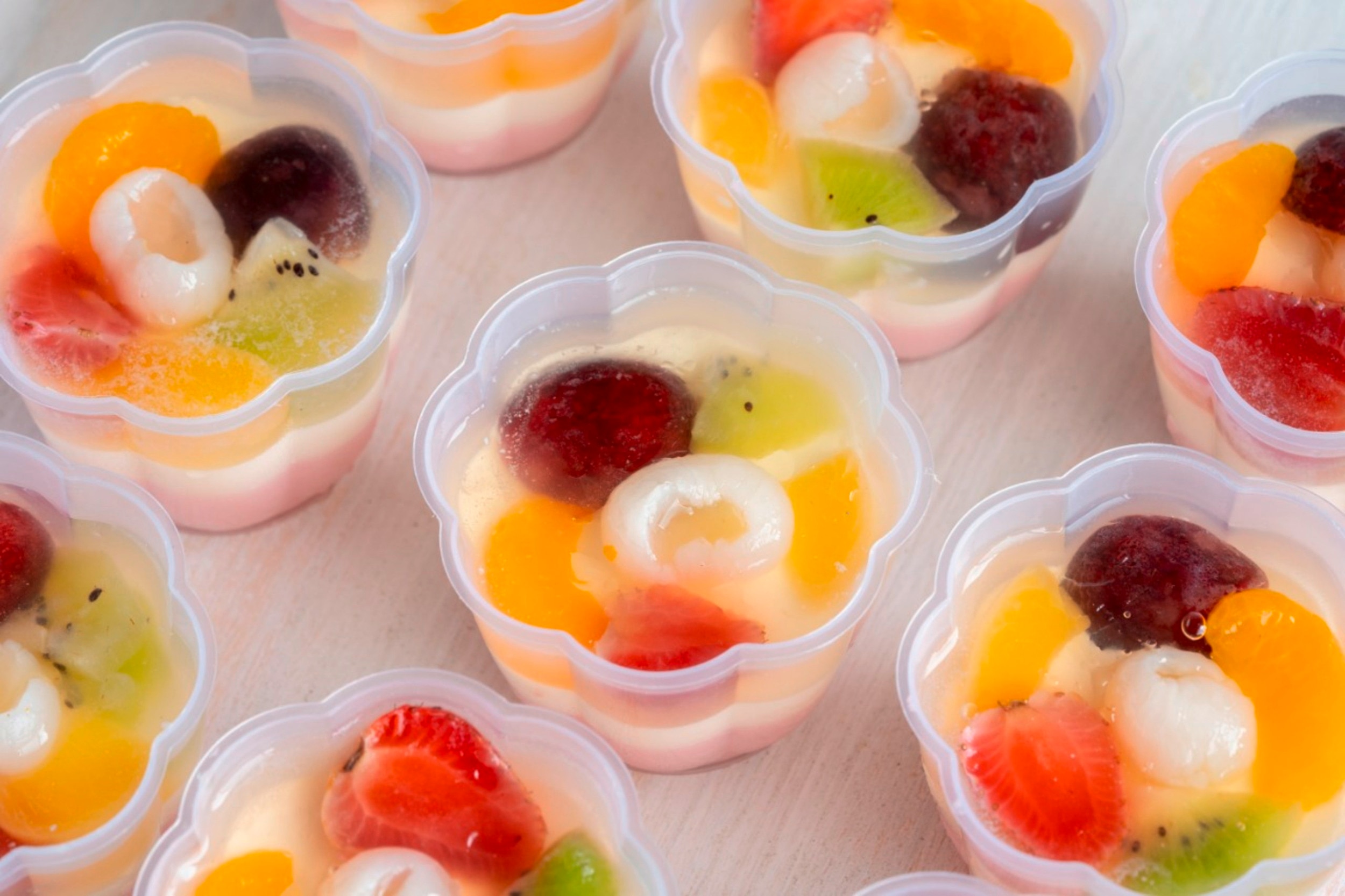 Individual serving cups of crema de fruta topped with strawberries, lychees, kiwis, and oranges