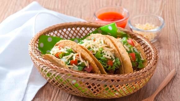 Hard-shell tacos with ground beef, tomatoes, lettuce, and cheese, served in a basket
