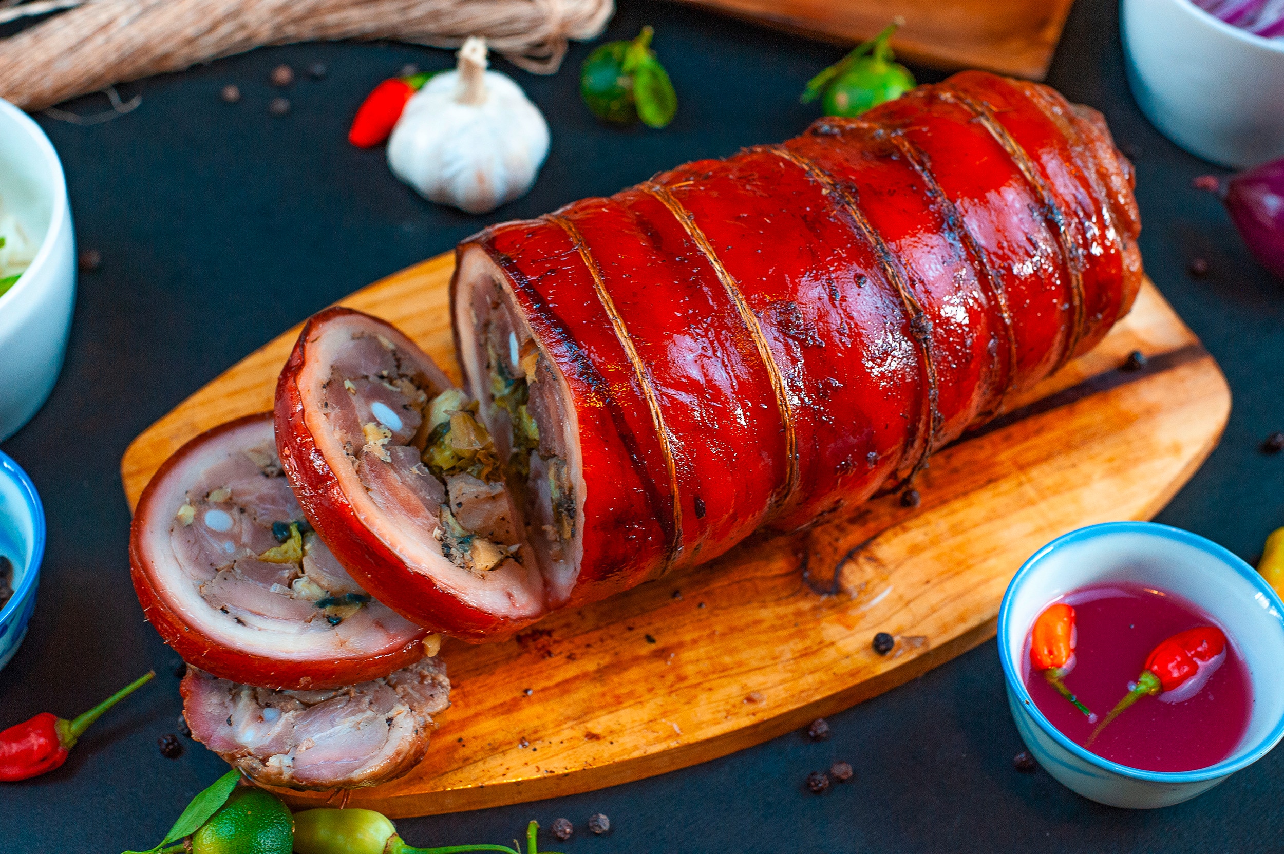 A wooden board with roasted and stuffed lechon belly roll