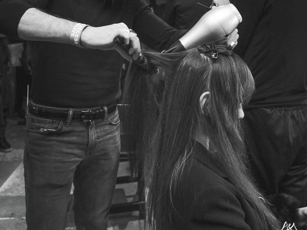A stylist using curling tongs on a model's long, dark curly hair.