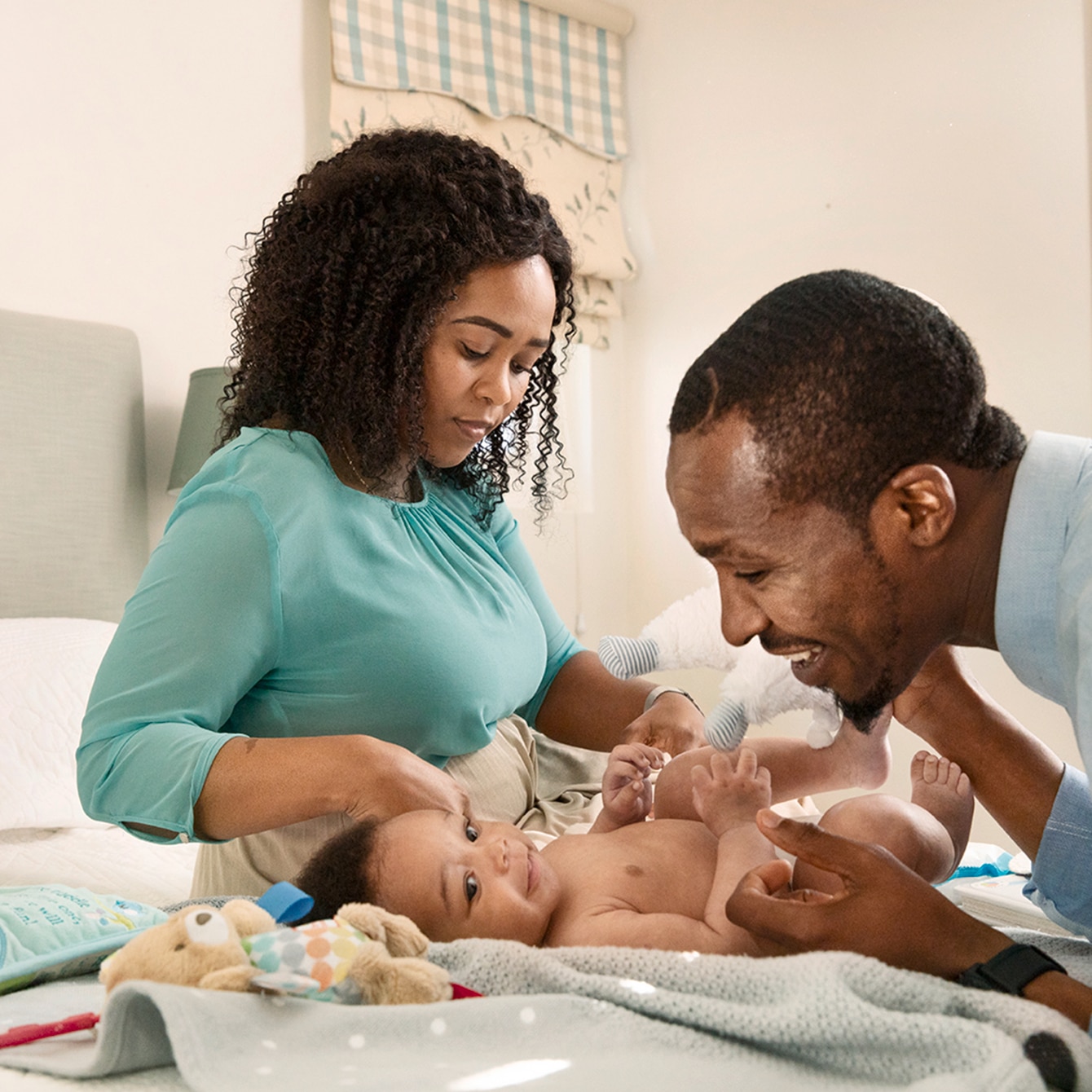 Mum and dad smiling at their baby whilst applying baby products