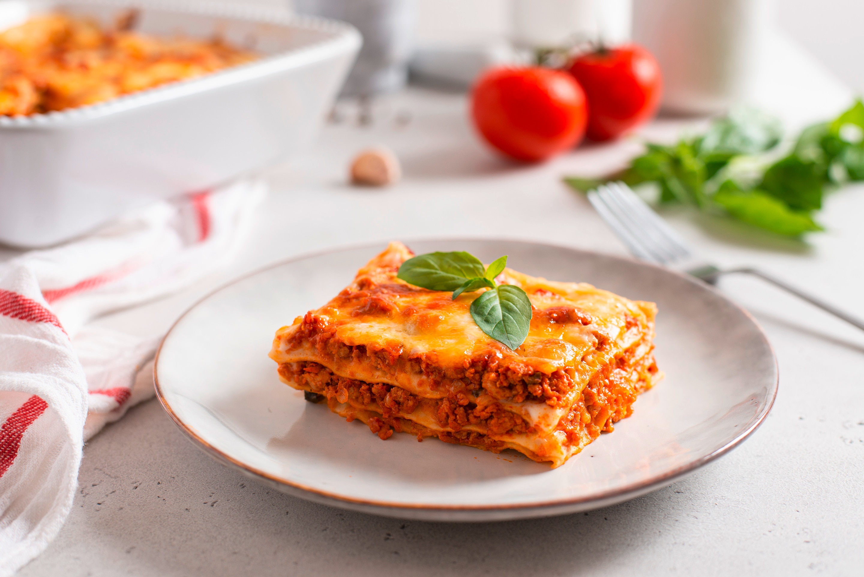 A plate with a slice of lasagna garnished with fresh basil leaves