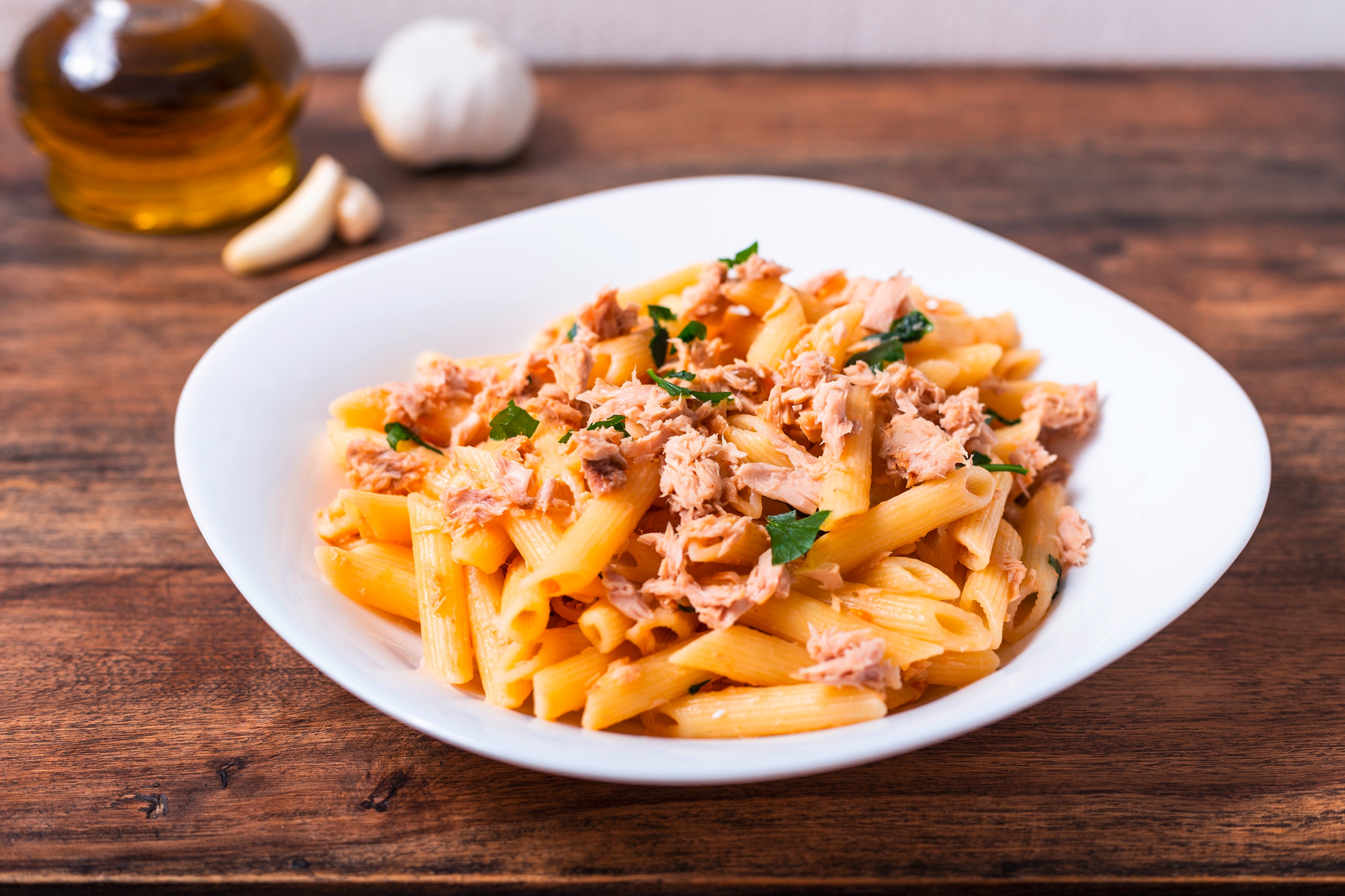 A plate of penne pasta with flaky tuna and fresh parsley