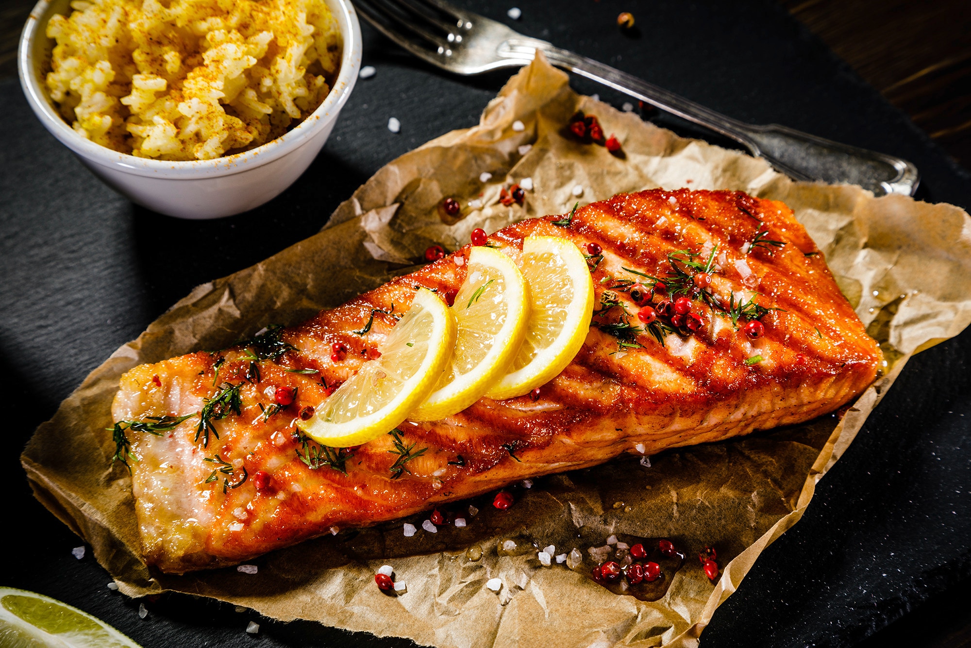 A baking tray with grilled salmon topped with herbs, spices, and lemon slices