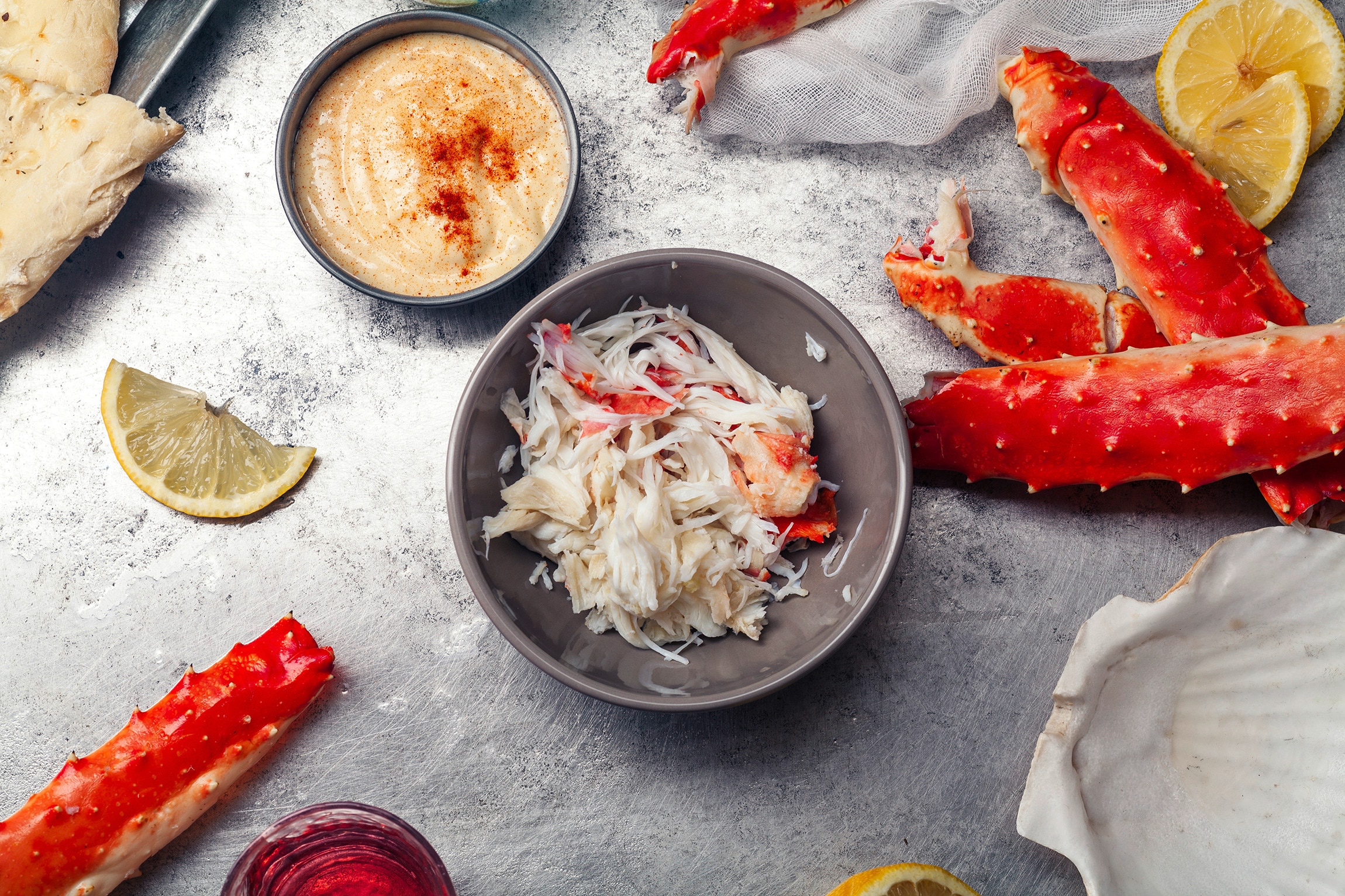 A bowl of shredded crab meat next to a saucer of aioli and crab legs