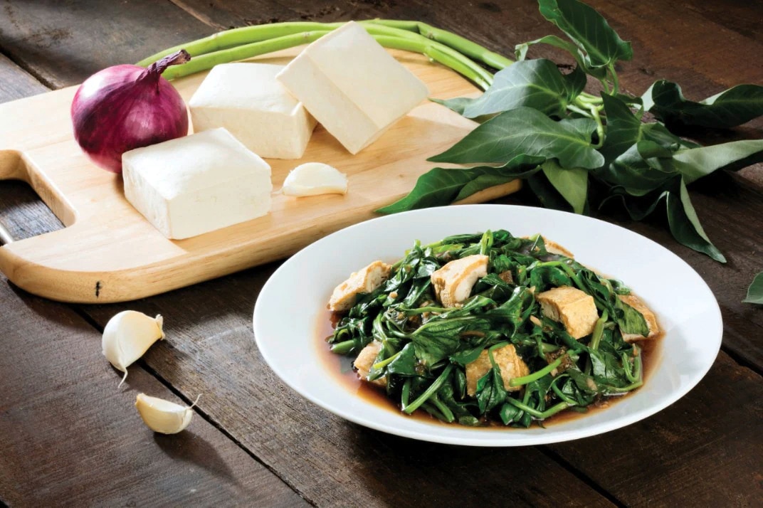 A plate of kangkong and tofu with oyster sauce surrounded with raw ingredients