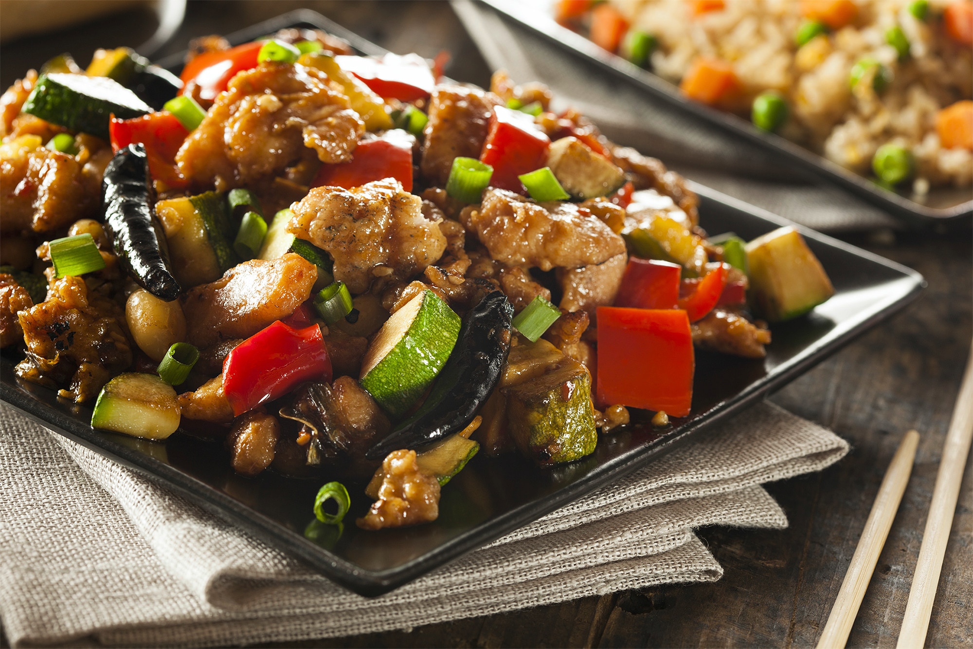 A plate of kung pao chicken with bell peppers, zucchini, and chilies
