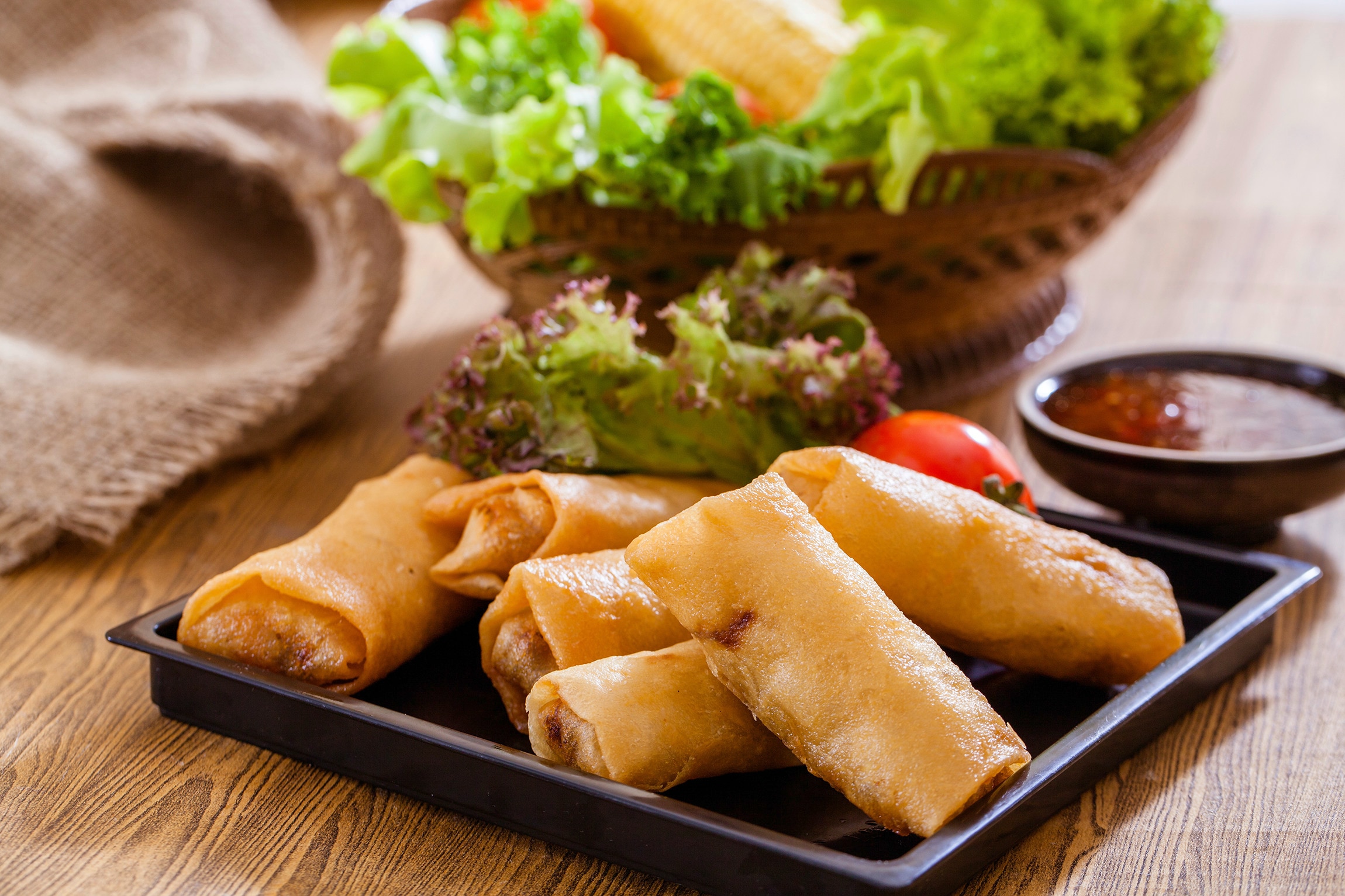 A plate of deep-fried spring rolls served with lettuce and a chili sauce