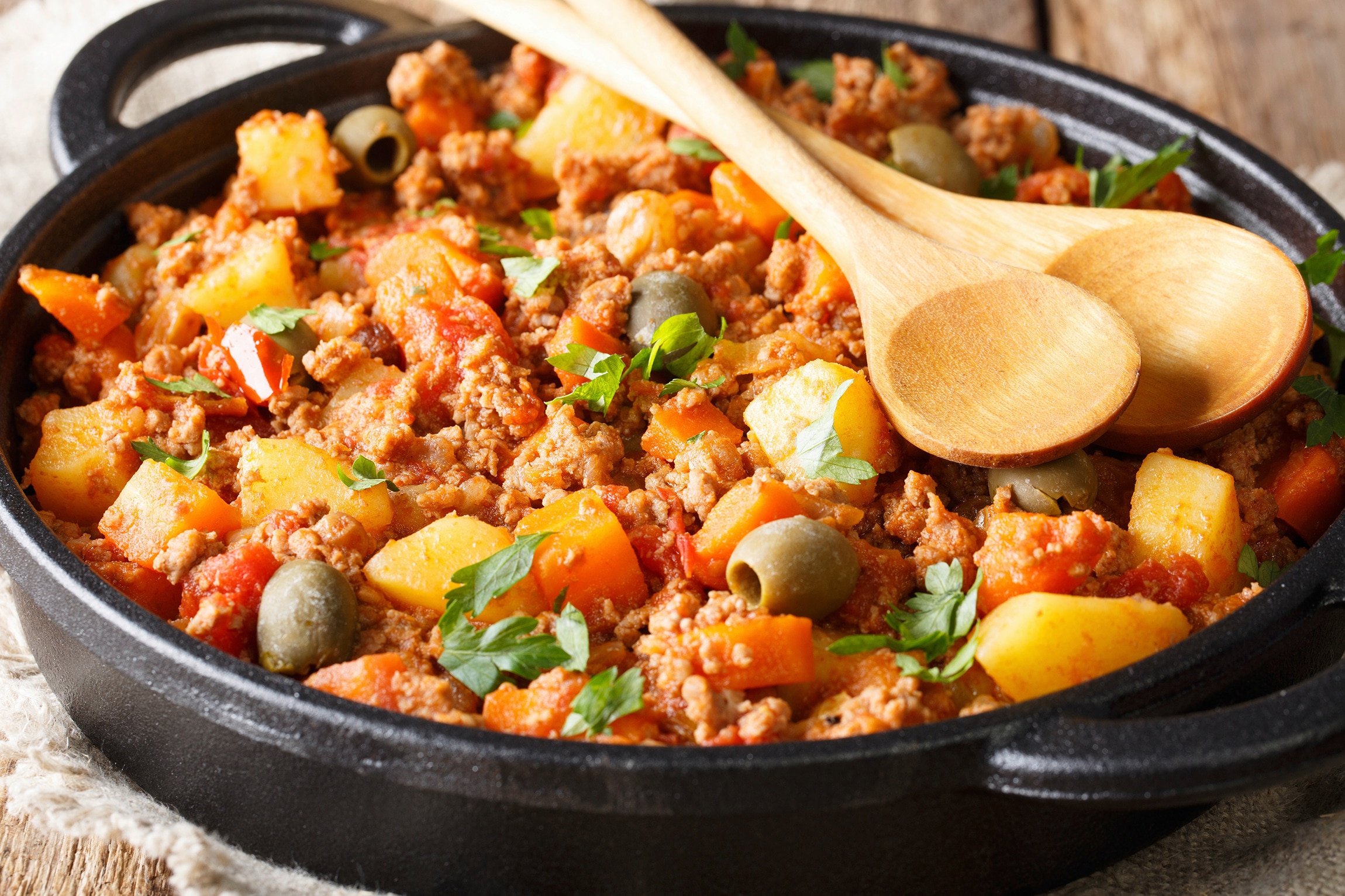 A skillet of picadillo with olives, carrots, potatoes, and bell peppers