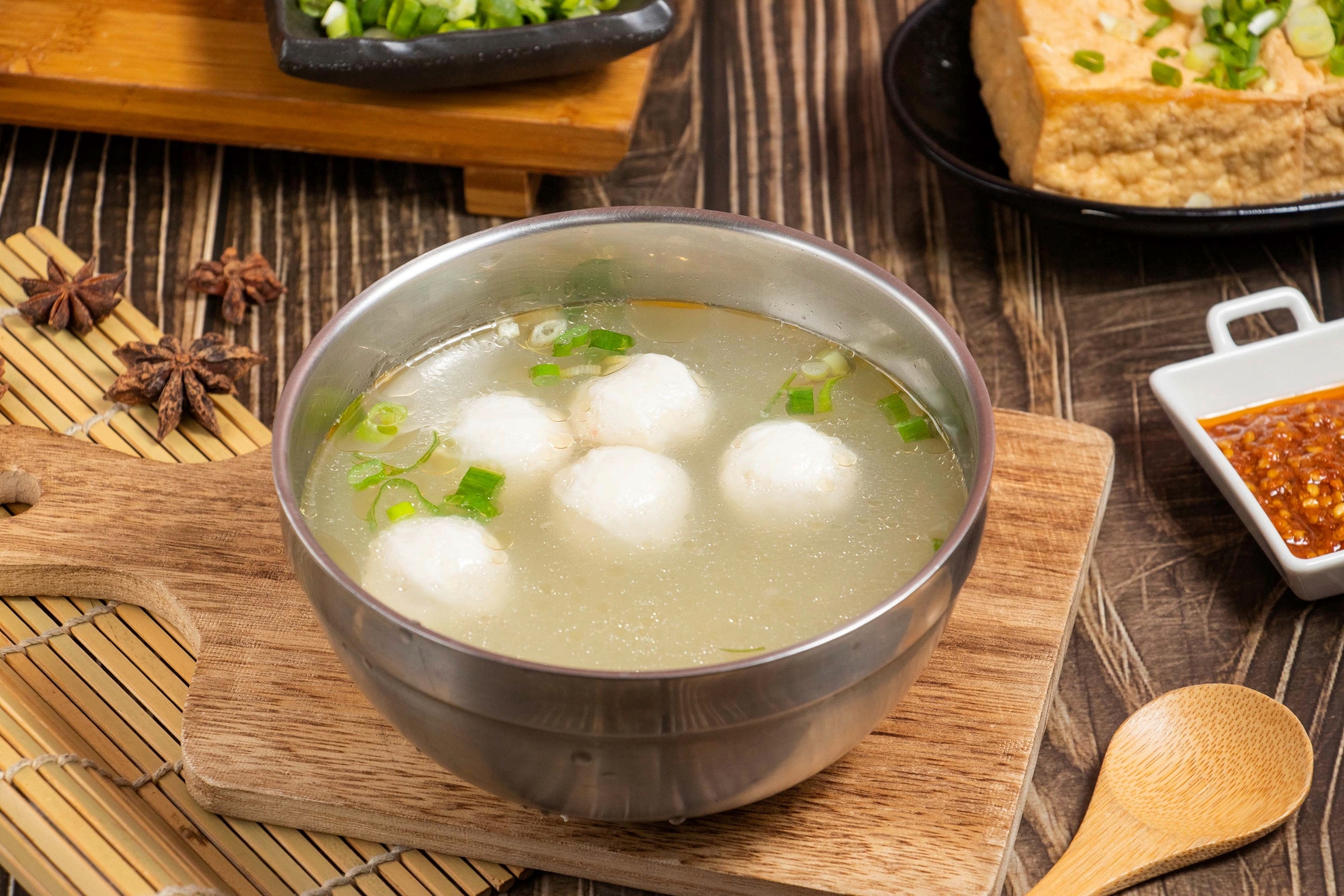 Squid balls in clear soup in a steel bowl, served with condiments
