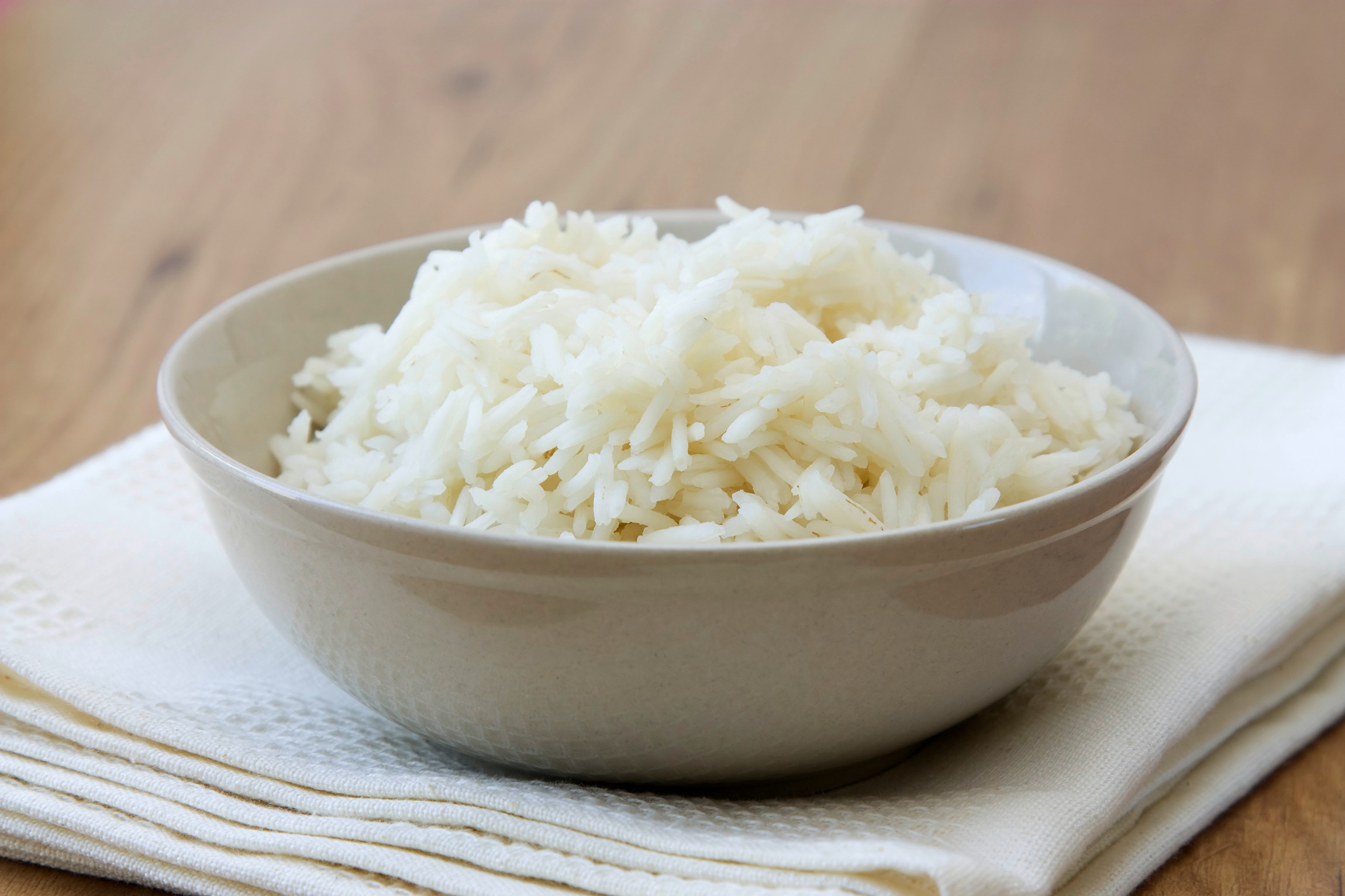 A bowl full of white rice served on a dish towel on a wooden table