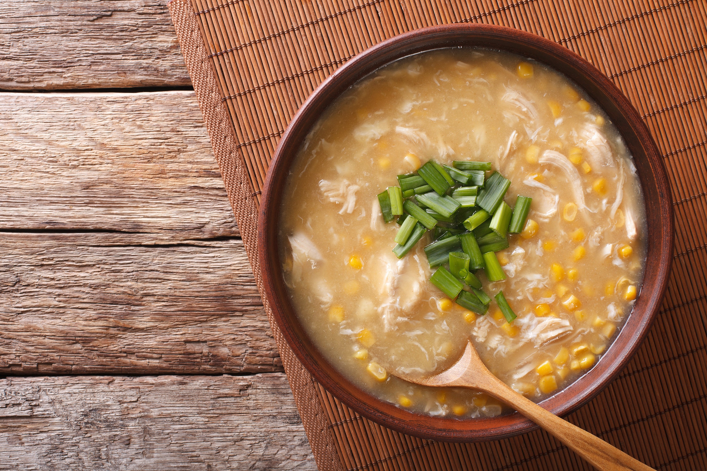 Crab and corn soup with chicken served in a bowl on a wooden mat