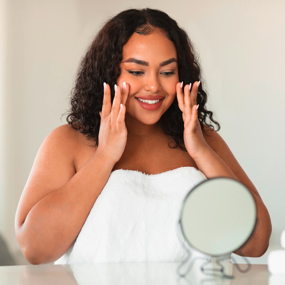 Beautiful woman touching her cheeks, looking in the mirror