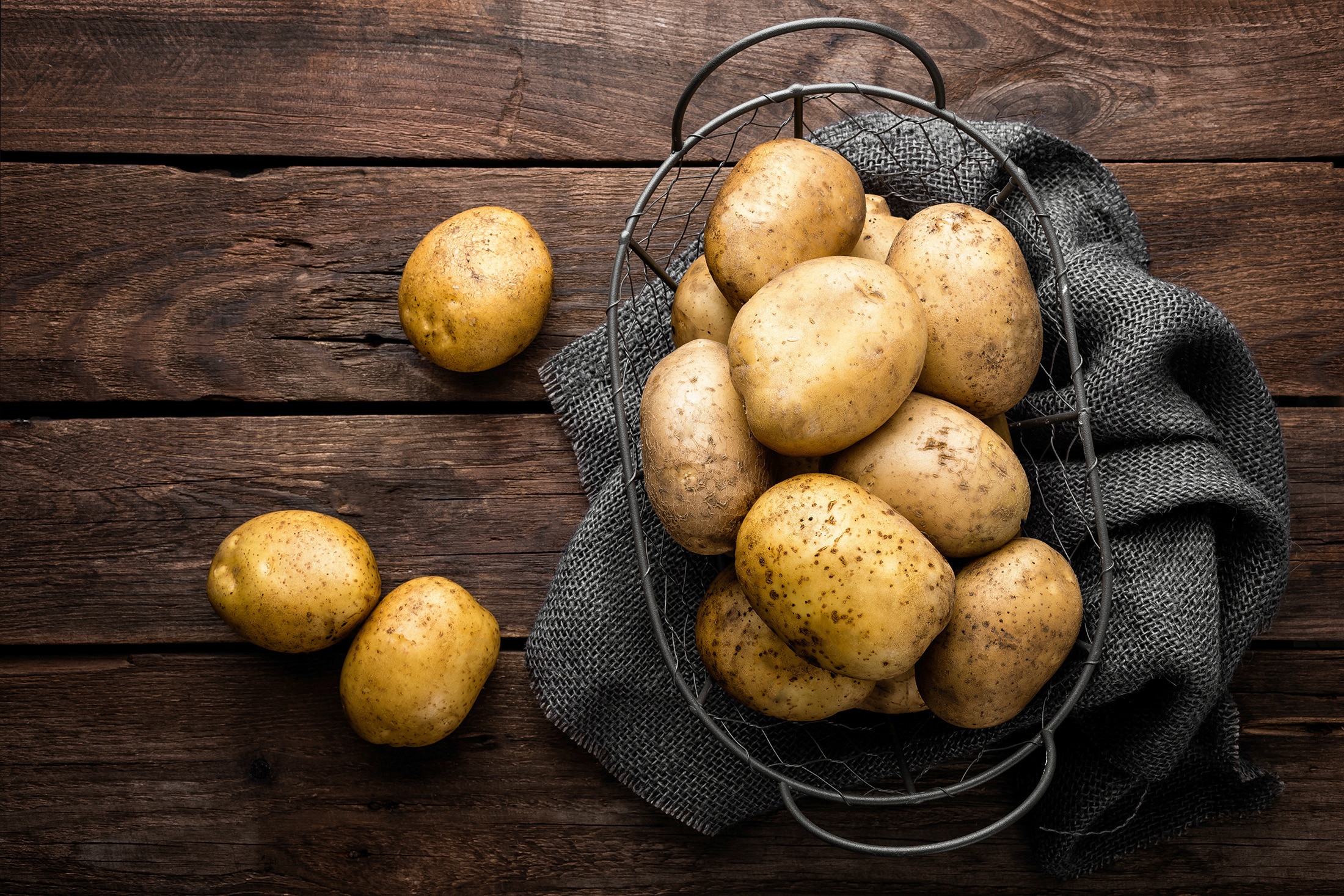 A metal basket full of potatoes on a wooden surface