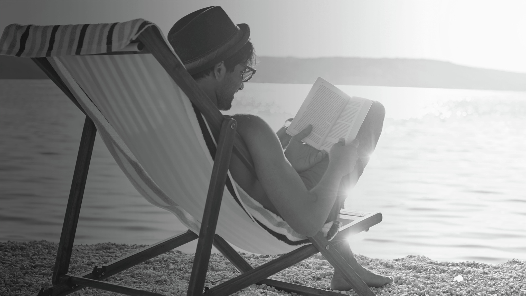 pria dengan topi membaca buku di pantai