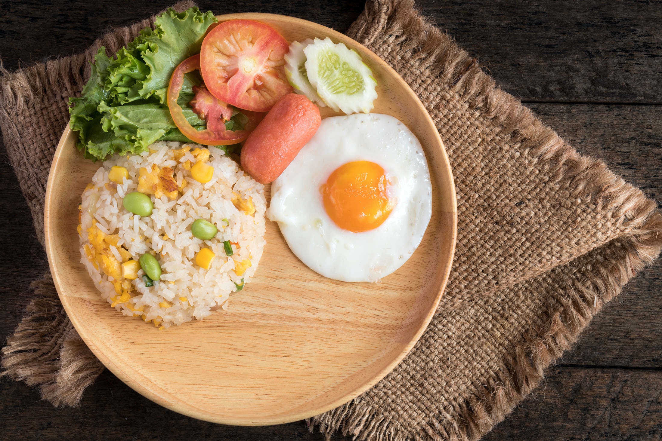 Egg fried rice with a side of fried egg, sausage, and vegetables