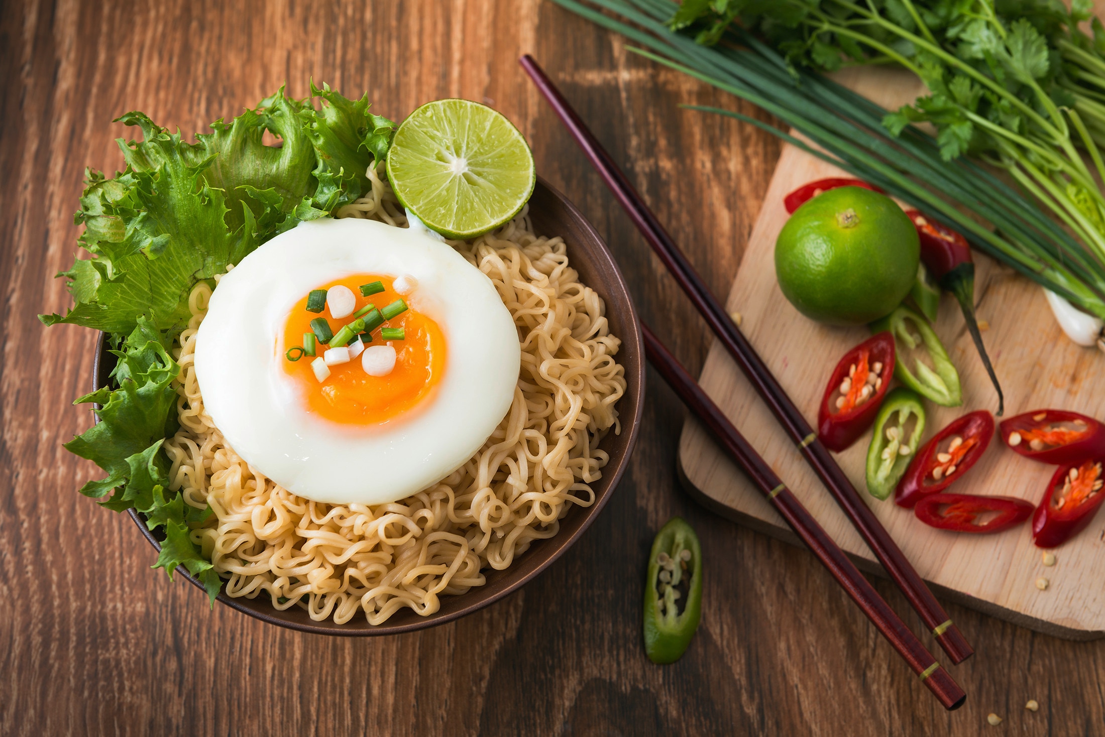 A bowl of instant noodles topped with egg and served with limes