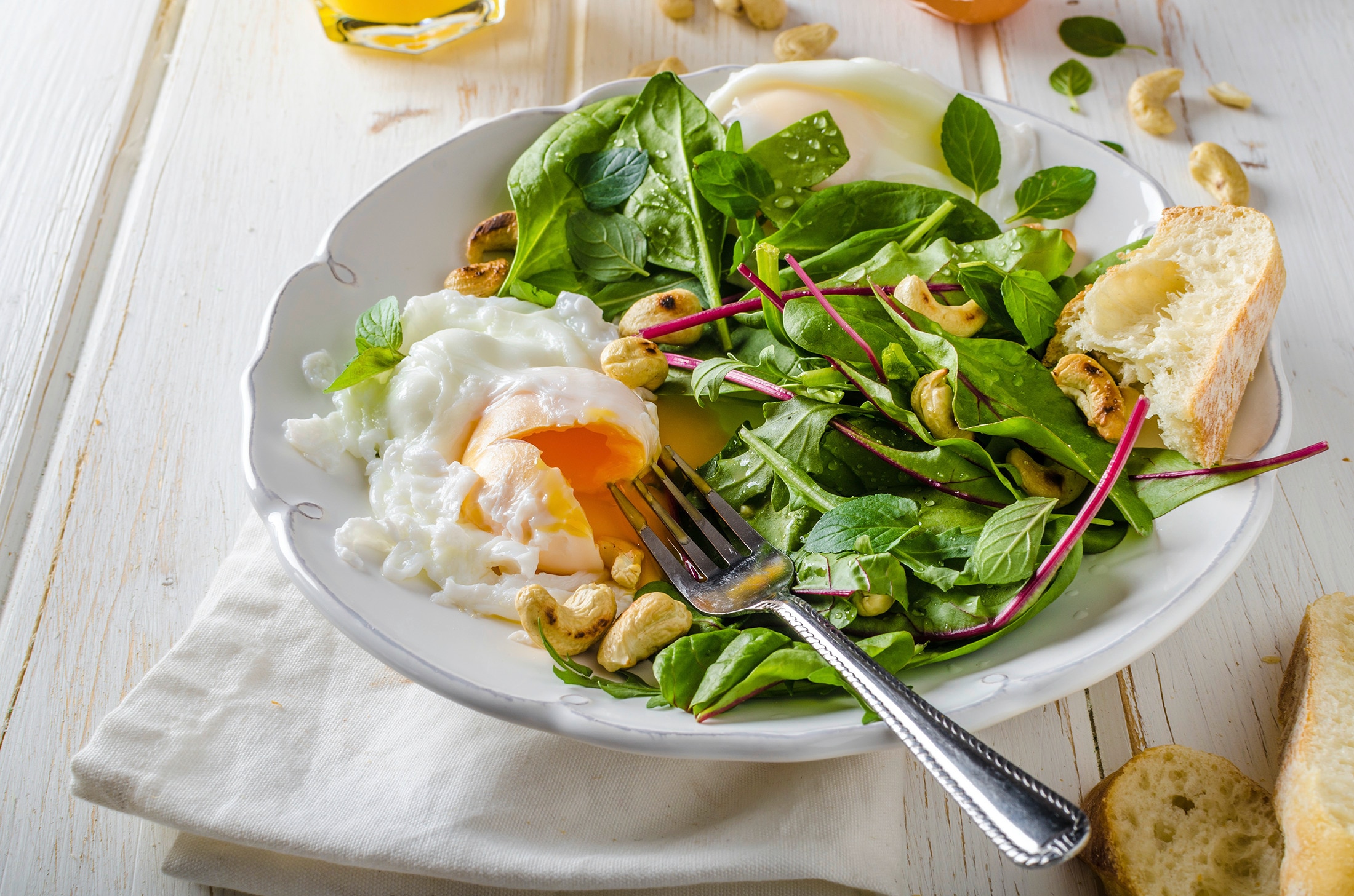 A fresh green salad with roasted cashews, a fried egg, and bread