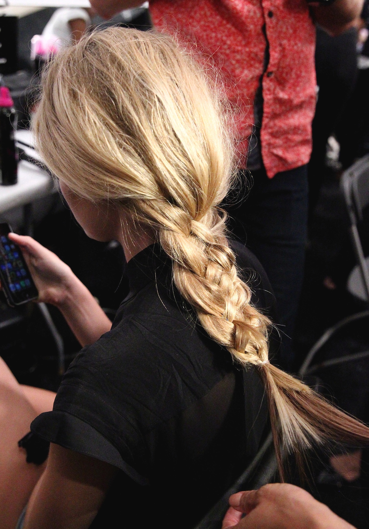 A blonde model sitting down backstage with her hair in a long, thick braid.